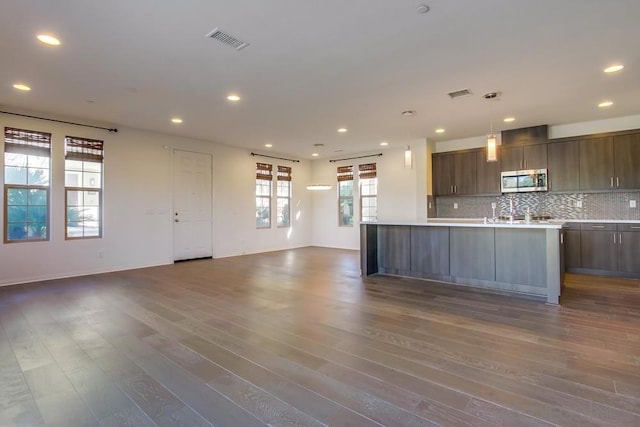 kitchen with decorative light fixtures, backsplash, an island with sink, and dark hardwood / wood-style floors