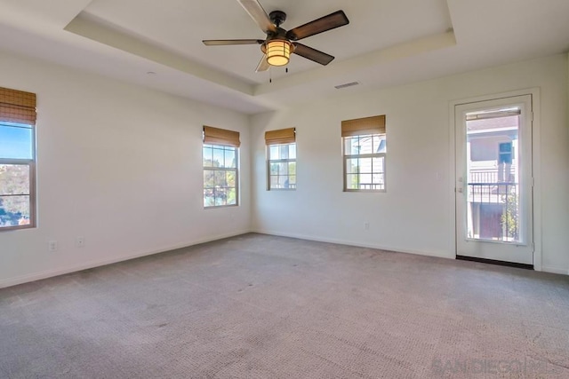 carpeted spare room featuring ceiling fan, a tray ceiling, and plenty of natural light