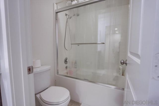 bathroom featuring toilet and bath / shower combo with glass door