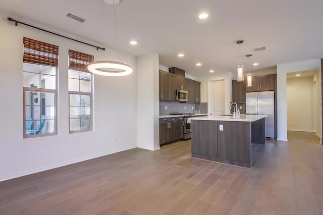 kitchen featuring decorative light fixtures, hardwood / wood-style flooring, an island with sink, dark brown cabinetry, and appliances with stainless steel finishes