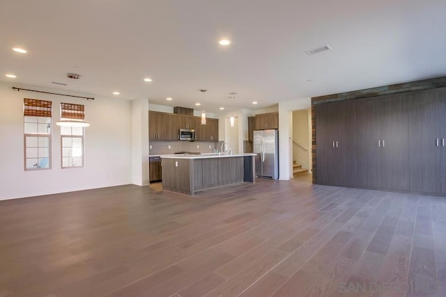 kitchen featuring stainless steel appliances, an island with sink, dark wood-type flooring, decorative backsplash, and decorative light fixtures