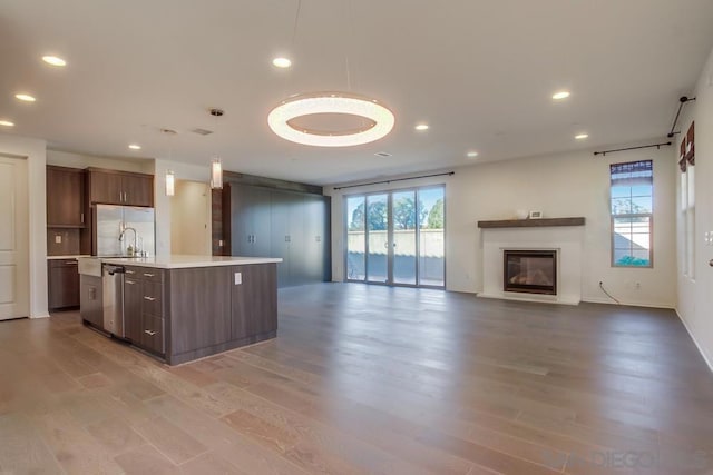 kitchen with appliances with stainless steel finishes, hanging light fixtures, hardwood / wood-style floors, and a kitchen island with sink