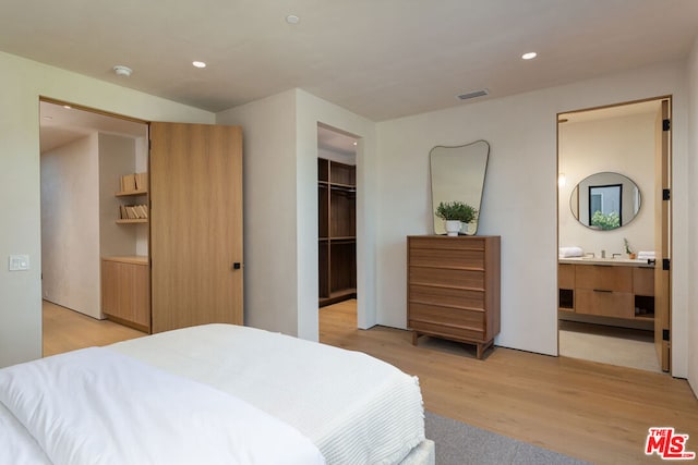 bedroom with light hardwood / wood-style floors, a walk in closet, a closet, and ensuite bath