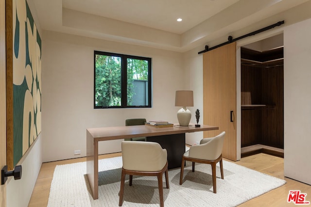 office featuring a raised ceiling, a barn door, and light hardwood / wood-style flooring