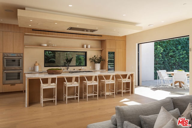 kitchen featuring double oven, light hardwood / wood-style flooring, light brown cabinetry, and a breakfast bar area