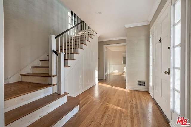 foyer entrance with a wealth of natural light, ornamental molding, and light hardwood / wood-style floors