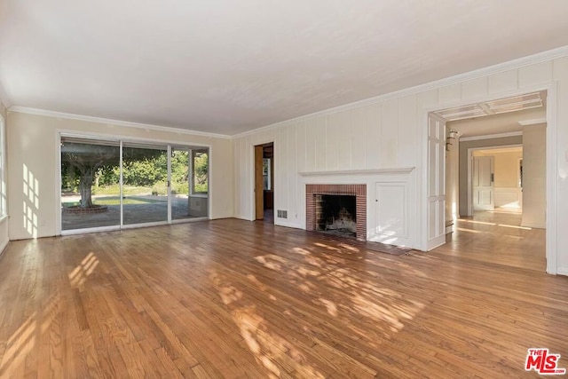 unfurnished living room with a brick fireplace, ornamental molding, and wood-type flooring