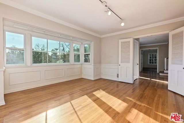 empty room with track lighting, wood-type flooring, plenty of natural light, and crown molding