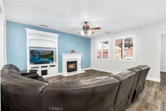 living room with ceiling fan, built in shelves, and dark hardwood / wood-style floors