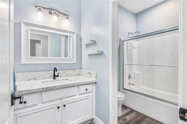 full bathroom featuring toilet, combined bath / shower with glass door, hardwood / wood-style floors, and vanity