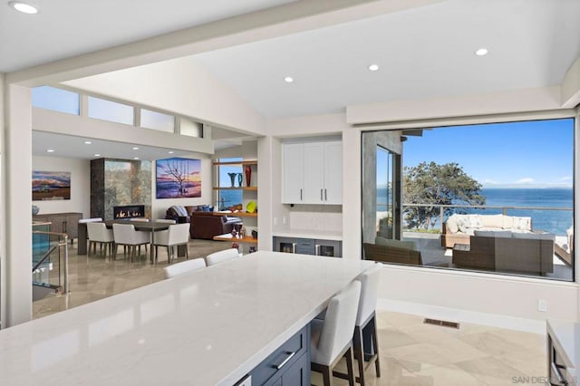 interior space with vaulted ceiling, light stone counters, a water view, a high end fireplace, and a breakfast bar