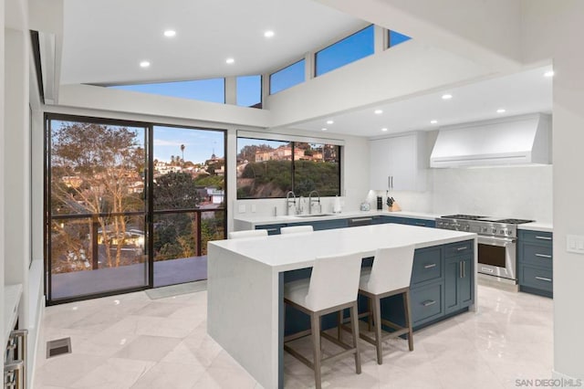 kitchen featuring vaulted ceiling, a center island, stainless steel stove, wall chimney exhaust hood, and sink