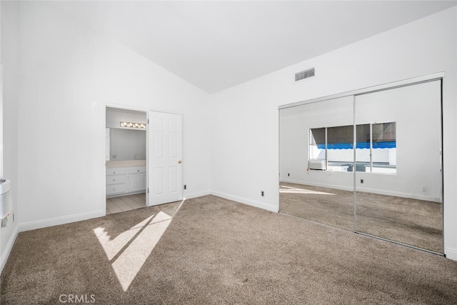 unfurnished bedroom featuring lofted ceiling, ensuite bathroom, a closet, and carpet flooring