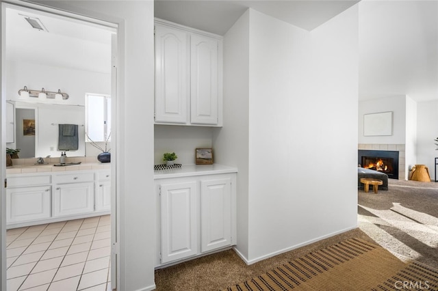 interior space with tile counters, white cabinetry, light carpet, and a fireplace