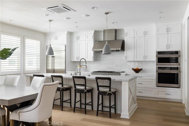 kitchen featuring a kitchen breakfast bar, decorative light fixtures, an island with sink, and wall chimney range hood