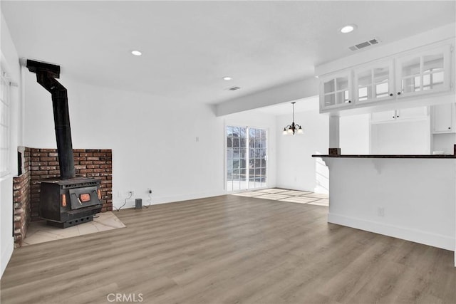 unfurnished living room featuring a wood stove, light hardwood / wood-style flooring, and a chandelier