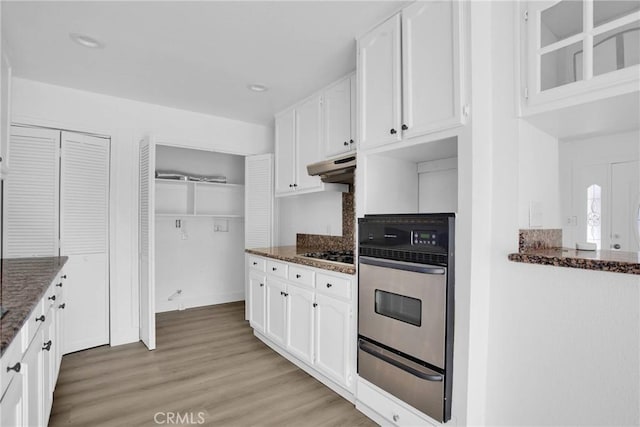 kitchen with white cabinetry, light hardwood / wood-style floors, appliances with stainless steel finishes, decorative backsplash, and dark stone counters