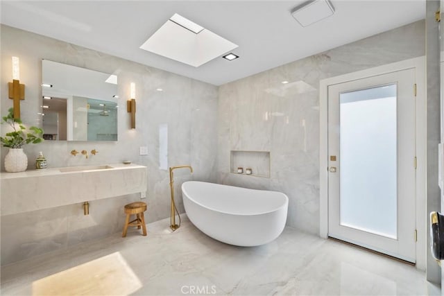 bathroom featuring sink, a bath, tile walls, and a skylight