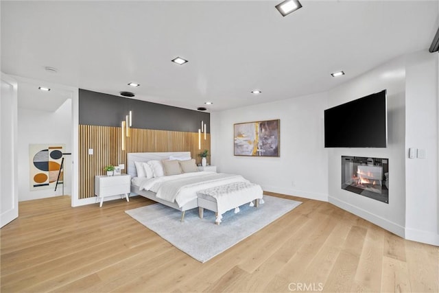 bedroom with a multi sided fireplace and light wood-type flooring