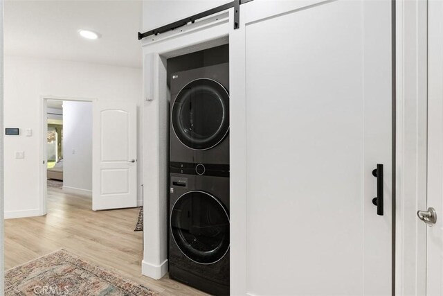 clothes washing area with light wood-type flooring, a barn door, and stacked washer and dryer