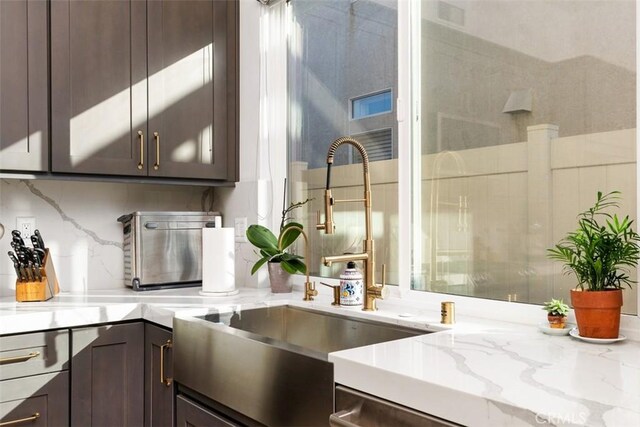 kitchen with light stone countertops, backsplash, dark brown cabinets, and sink