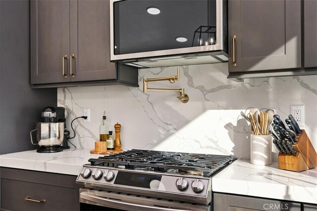 kitchen with light stone counters, dark brown cabinets, appliances with stainless steel finishes, and tasteful backsplash