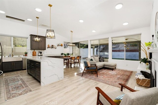 kitchen with light wood-type flooring, light stone countertops, pendant lighting, dark brown cabinetry, and sink