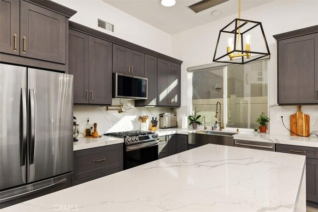 kitchen with stainless steel appliances, light stone countertops, pendant lighting, decorative backsplash, and sink