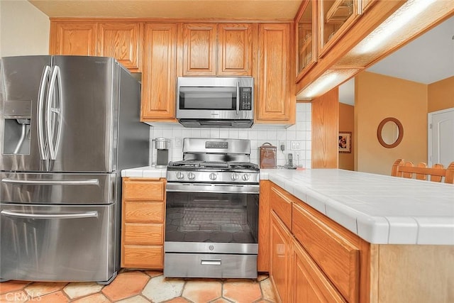 kitchen featuring tile countertops, kitchen peninsula, decorative backsplash, light tile patterned flooring, and stainless steel appliances