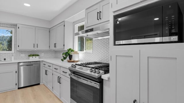 kitchen featuring appliances with stainless steel finishes, wall chimney range hood, a wealth of natural light, and white cabinetry