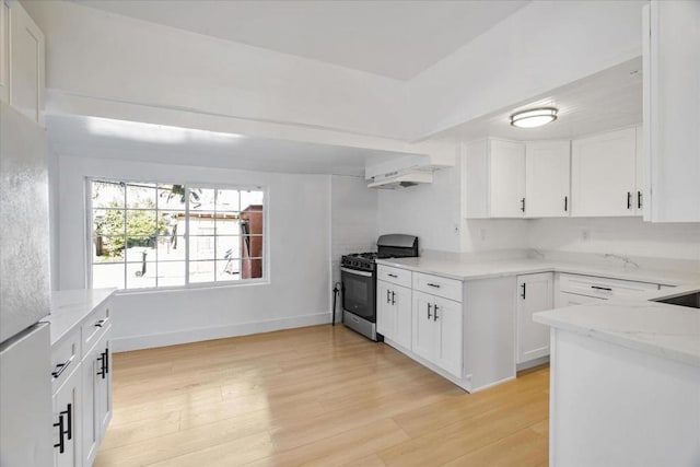 kitchen featuring light stone countertops, stainless steel gas range, white cabinetry, white refrigerator, and light wood-type flooring