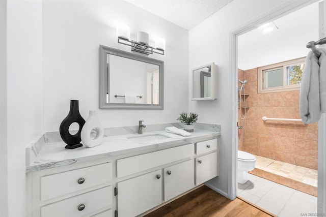 bathroom featuring toilet, vanity, a tile shower, hardwood / wood-style flooring, and a textured ceiling