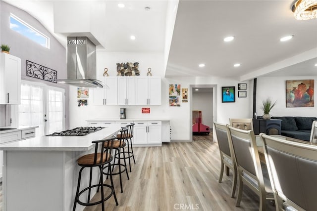 kitchen featuring a center island, island exhaust hood, light hardwood / wood-style flooring, stainless steel gas cooktop, and white cabinets