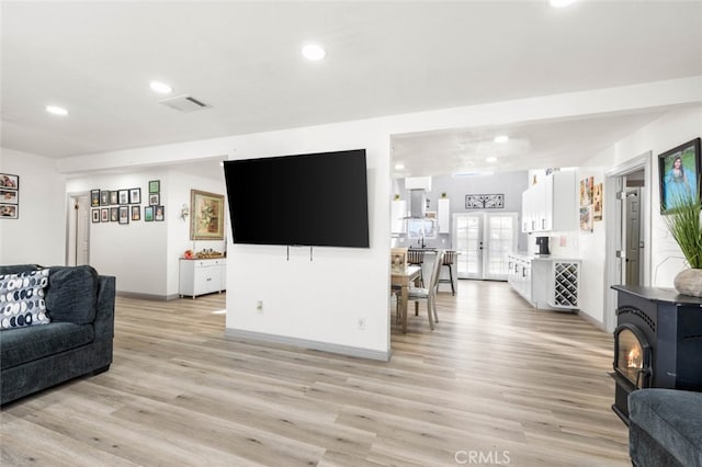 living room with light hardwood / wood-style floors, a wood stove, and french doors