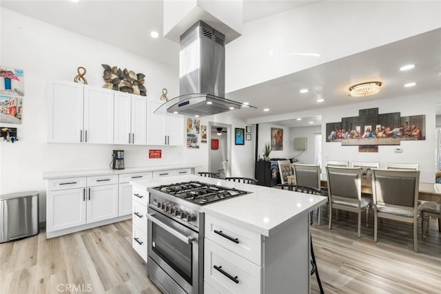 kitchen with island exhaust hood, white cabinetry, and stainless steel range