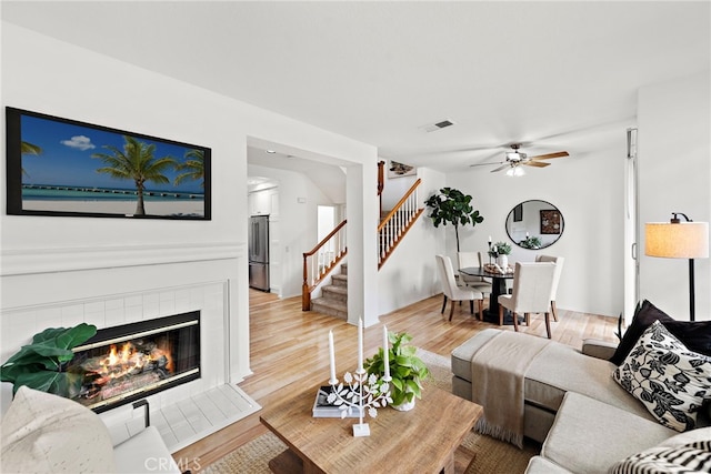 living room featuring ceiling fan, hardwood / wood-style floors, and a tile fireplace