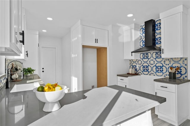 kitchen with white cabinetry, sink, wall chimney range hood, and backsplash