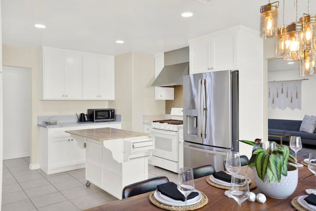 kitchen featuring white cabinets, appliances with stainless steel finishes, wall chimney range hood, and pendant lighting