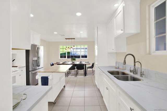 kitchen with light stone countertops, stainless steel fridge, light tile patterned floors, white cabinets, and sink