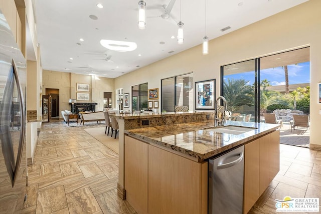 kitchen featuring a large island, sink, pendant lighting, ceiling fan, and light stone countertops