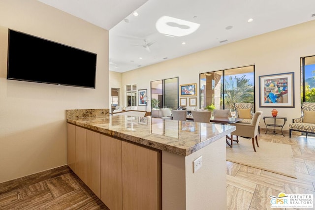 kitchen featuring light brown cabinets, kitchen peninsula, dark parquet floors, ceiling fan, and light stone countertops