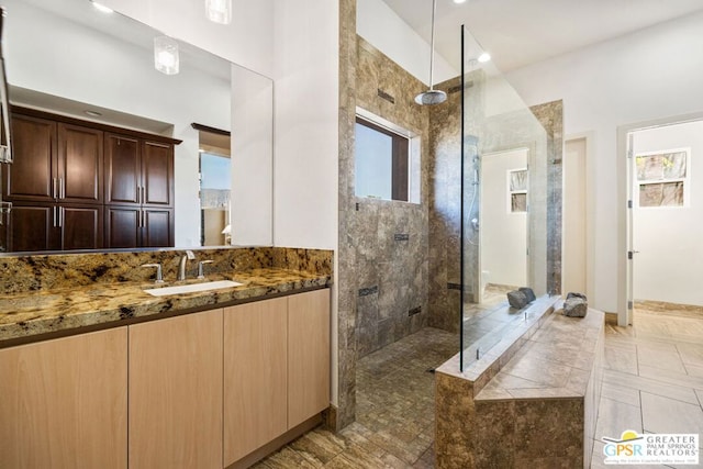 bathroom with a tile shower, vanity, and plenty of natural light