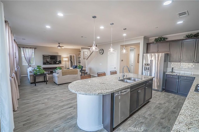 kitchen featuring sink, tasteful backsplash, decorative light fixtures, stainless steel appliances, and a kitchen island with sink