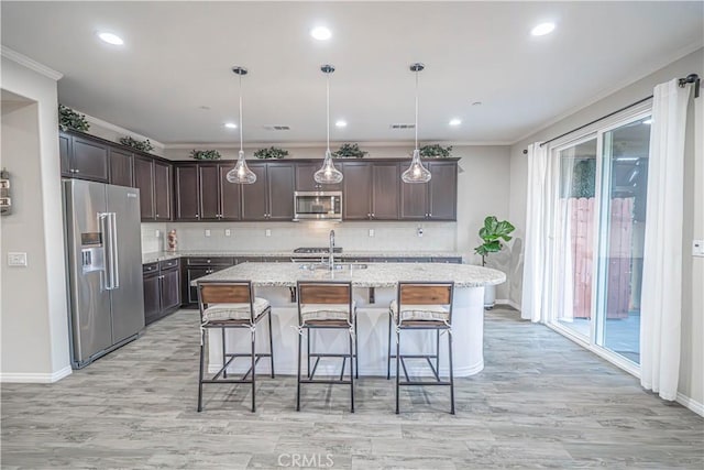 kitchen featuring pendant lighting, dark brown cabinets, stainless steel appliances, and a center island with sink