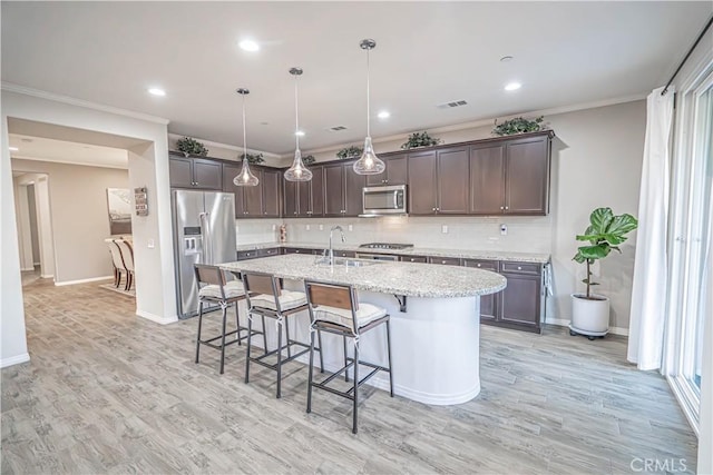 kitchen featuring dark brown cabinetry, sink, decorative light fixtures, stainless steel appliances, and a kitchen island with sink