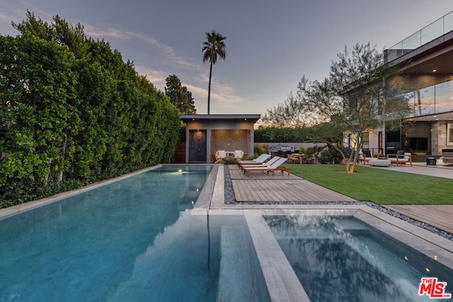 pool at dusk featuring a lawn and a wooden deck