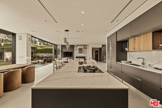 kitchen featuring sink, decorative light fixtures, light stone counters, black gas cooktop, and a kitchen island