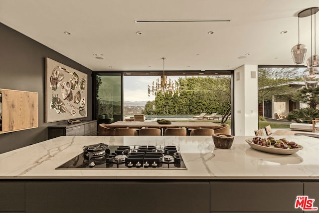 kitchen featuring a chandelier, hanging light fixtures, light stone countertops, expansive windows, and black gas stovetop