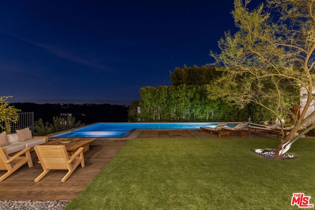 pool at night featuring a lawn