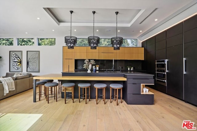 kitchen featuring tasteful backsplash, a raised ceiling, pendant lighting, and a kitchen bar